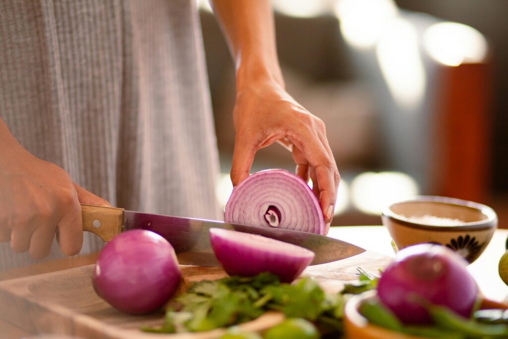 Hands slicing a red onion on a cutting board, showcasing fresh ingredients.